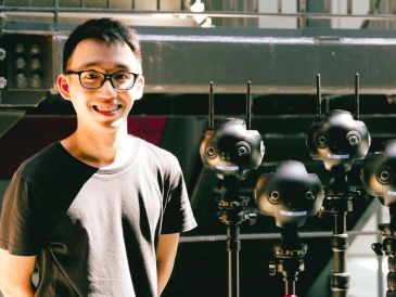Young man smiling beside high-tech cameras.
