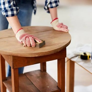 Person sanding a wooden round table wearing gloves.