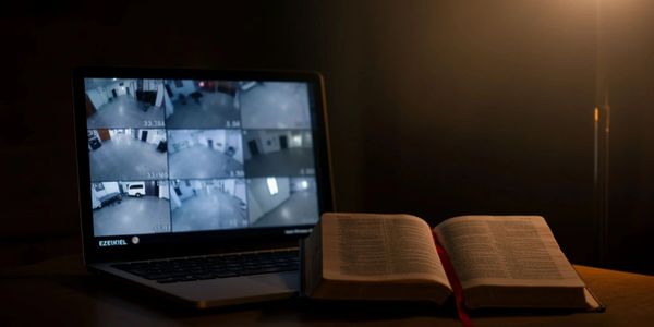 Open book beside a laptop displaying security camera feeds in dim light.