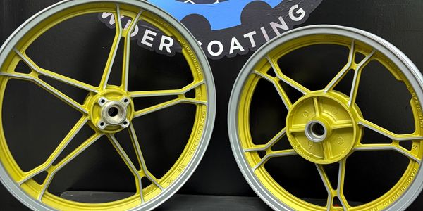 Two yellow and silver motorcycle wheels against a Dynamic Coatings wall.