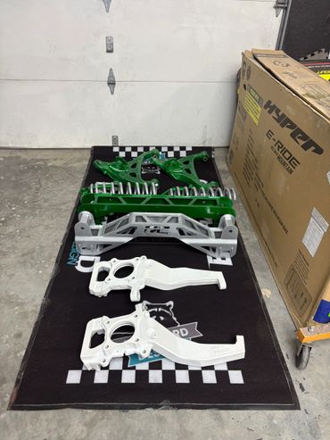 Painted automotive suspension parts neatly arranged on a black mat in a garage.