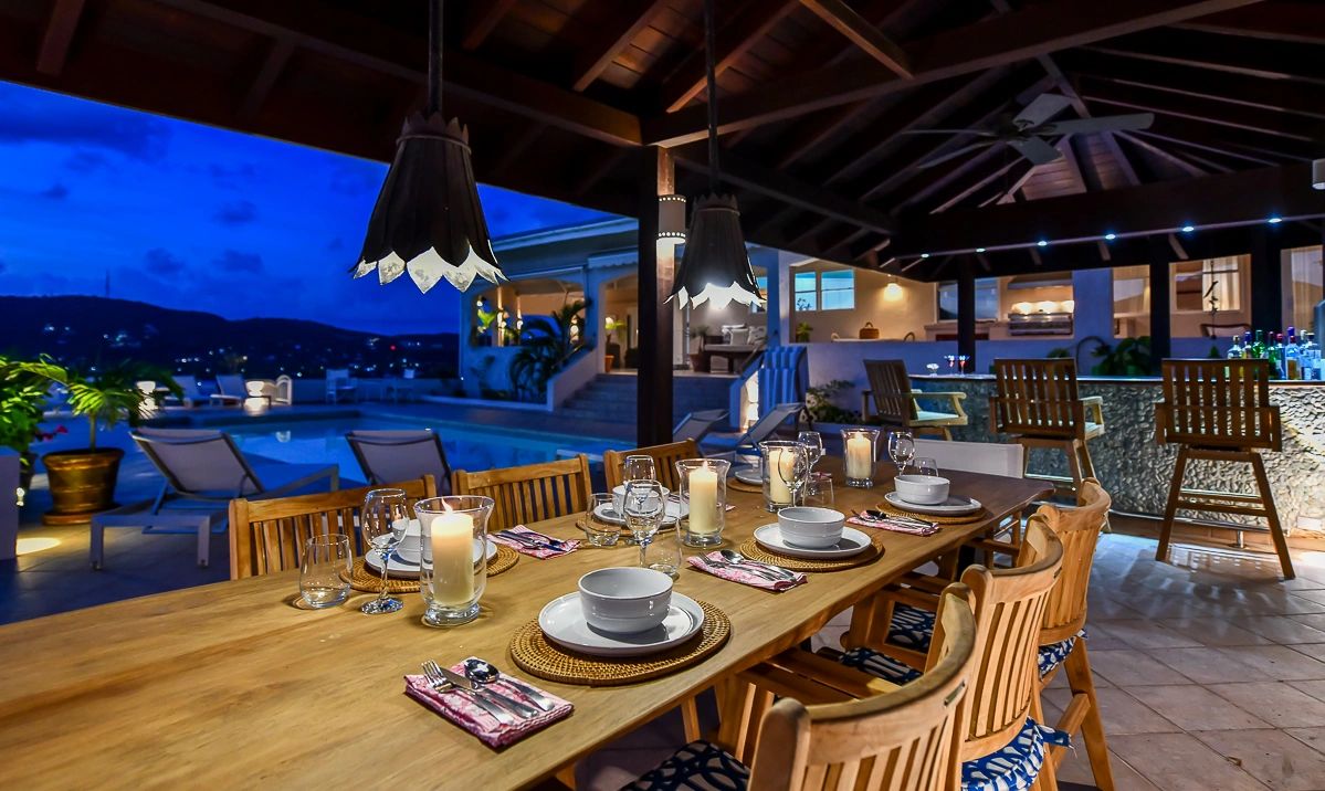 Bluff House covered bar area by the pool with teak dining table set for dinner by candlelight
