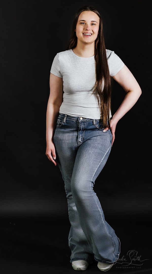 Smiling woman in a white t-shirt and blue jeans posing against a black background.