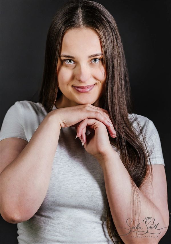 Young woman with long brown hair smiling gently in a white shirt.