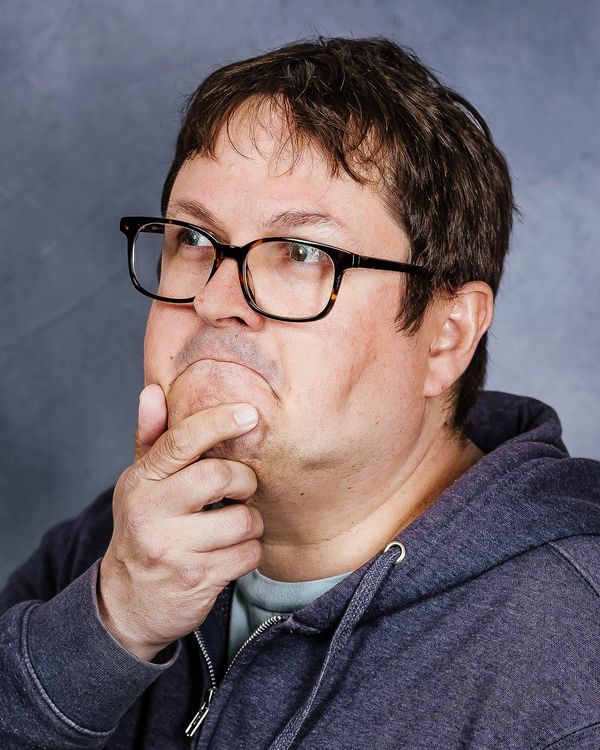 Man with glasses thoughtfully touching his chin, looking upwards.