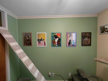 A green wall with five colorful cat paintings and a cat climbing structure.