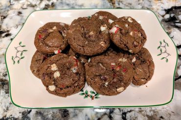 Plate of chocolate cookies with white and red chunks on a festive dish.