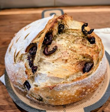 Round loaf of crusty bread with olives and herbs baked inside.