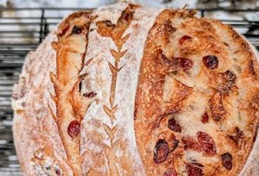 Freshly baked artisan bread with cranberries and decorative scoring.
