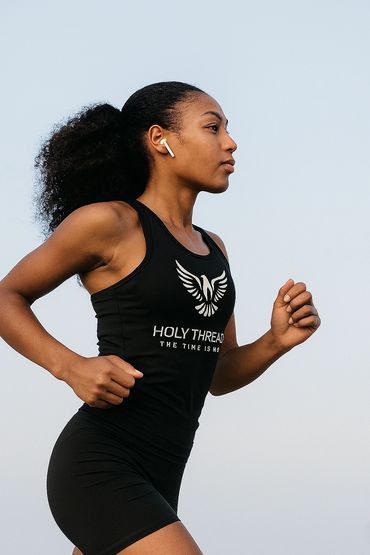 Woman running outdoors wearing wireless earbuds and a black workout outfit.