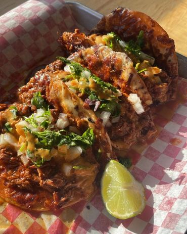 Delicious tacos with meat, cilantro, onions, and a lime wedge.