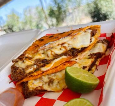 Two cheesy quesabirria tacos with lime wedges.