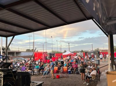 Outdoor gathering with people seated under a covered area. Busy food trucks in the background
