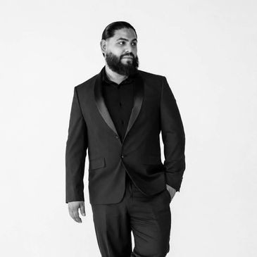 Hombre con traje negro y barba mirando hacia un lado.