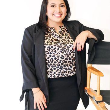 Mujer sonriente con chaqueta negra y blusa de estampado animal.