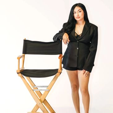 Mujer joven con chaqueta negra junto a una silla de director.