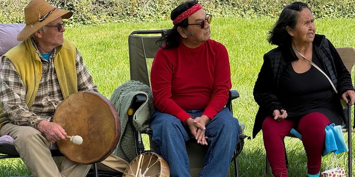 Three people sitting outdoors, one holding a drum.