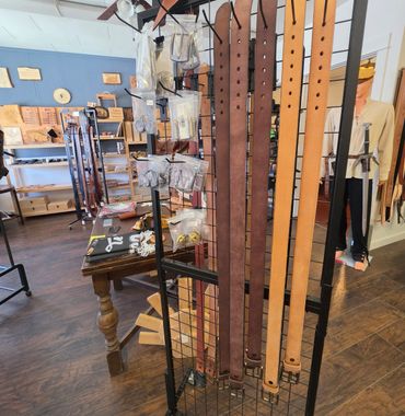 Leather belts and buckles on display in a store with a mannequin in the background.