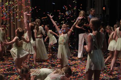 Young dancers celebrate on stage with colorful confetti falling around them.