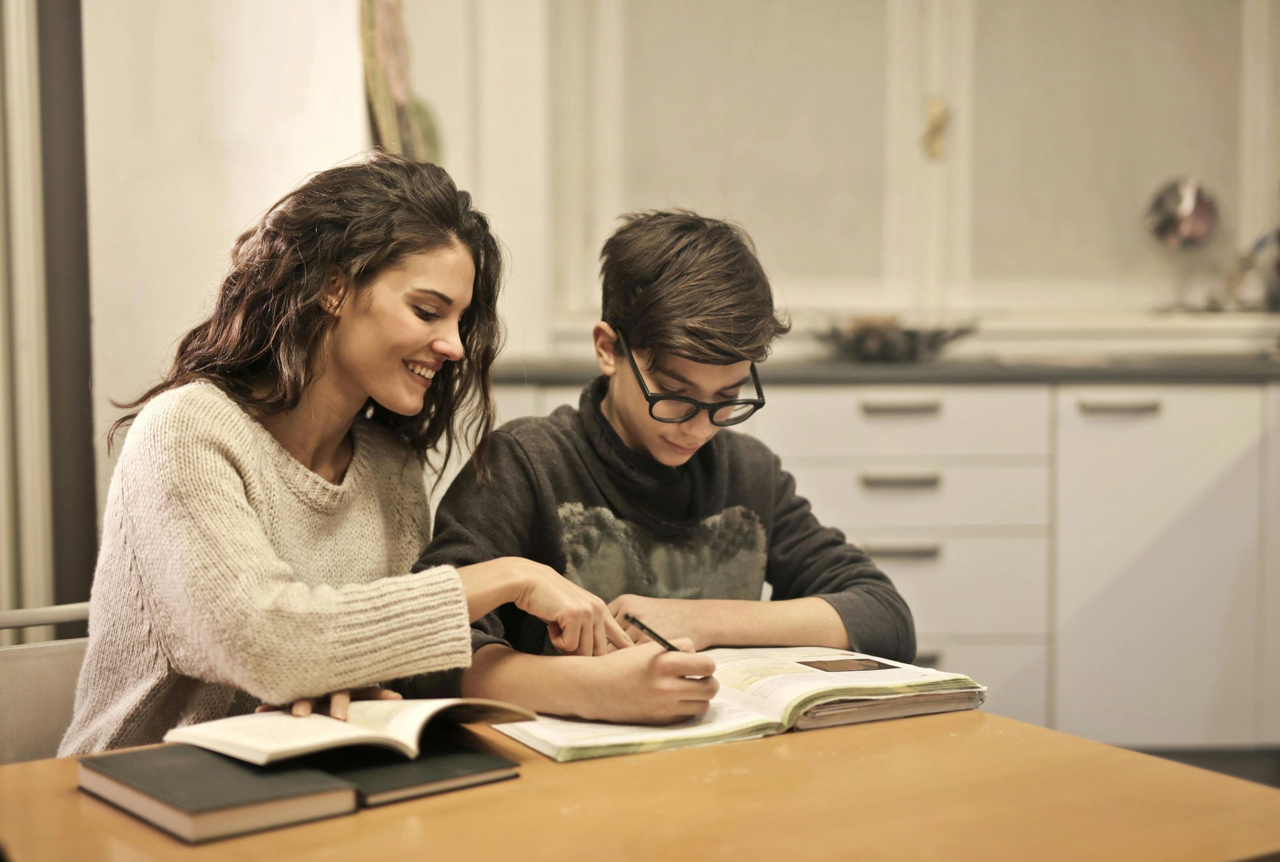 A woman helps a boy with homework at a table indoors.