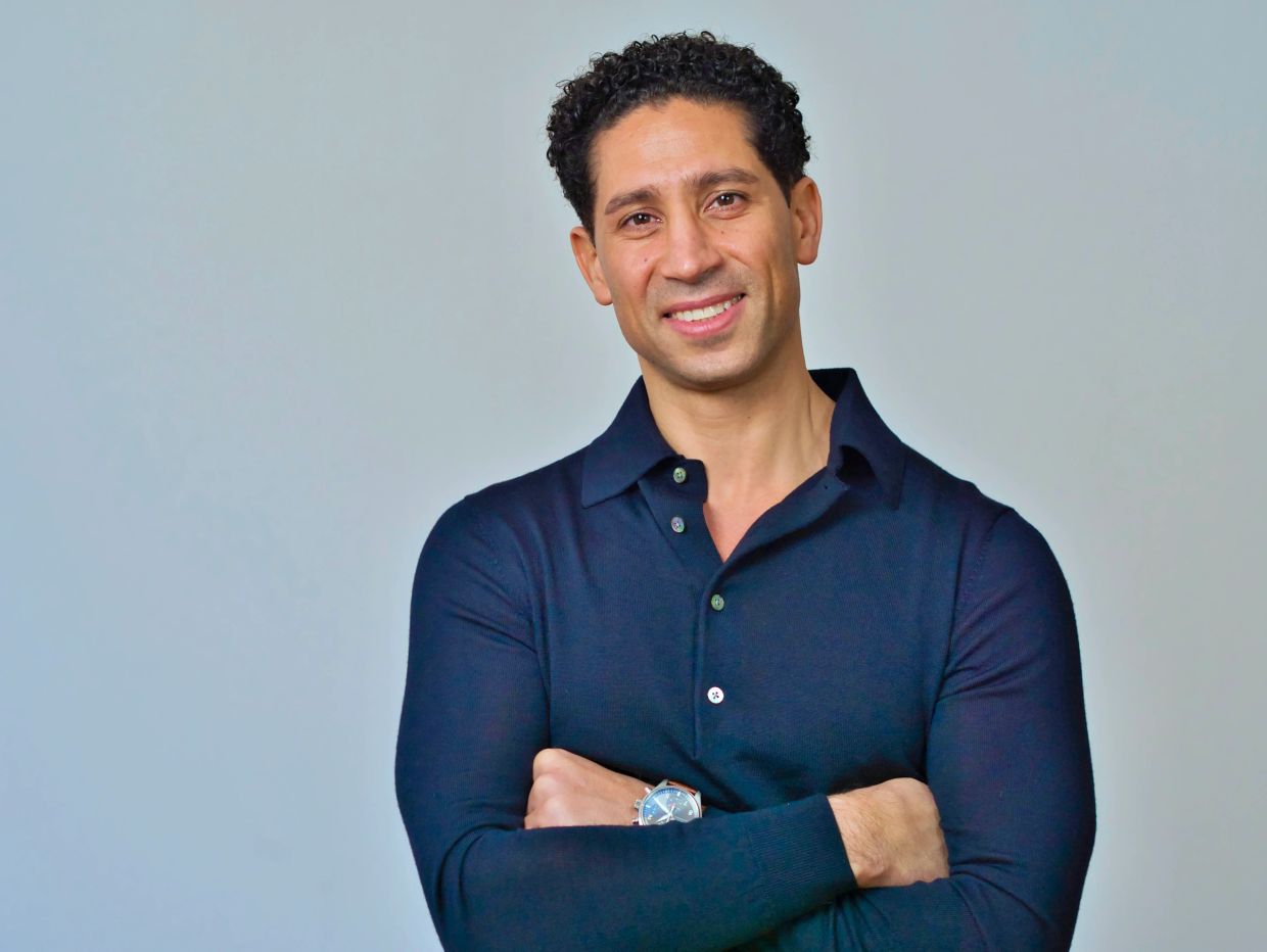 Man with arms crossed smiling against a plain background.