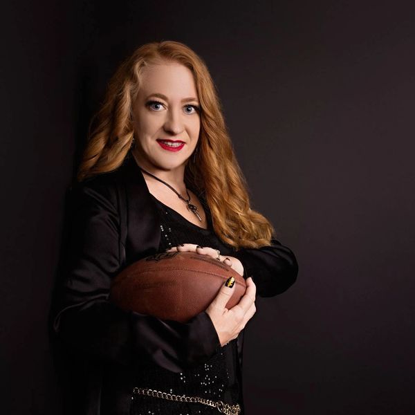 Woman holding an American football against a dark background.