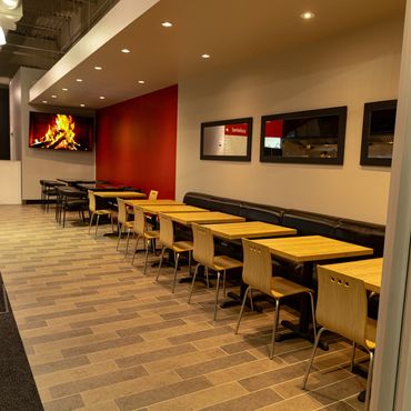 Salle à manger moderne avec tables et chaises en bois, et télévision diffusant une image de cheminée.
