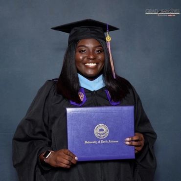 Smiling graduate in cap and gown holding diploma from University of North Alabama.