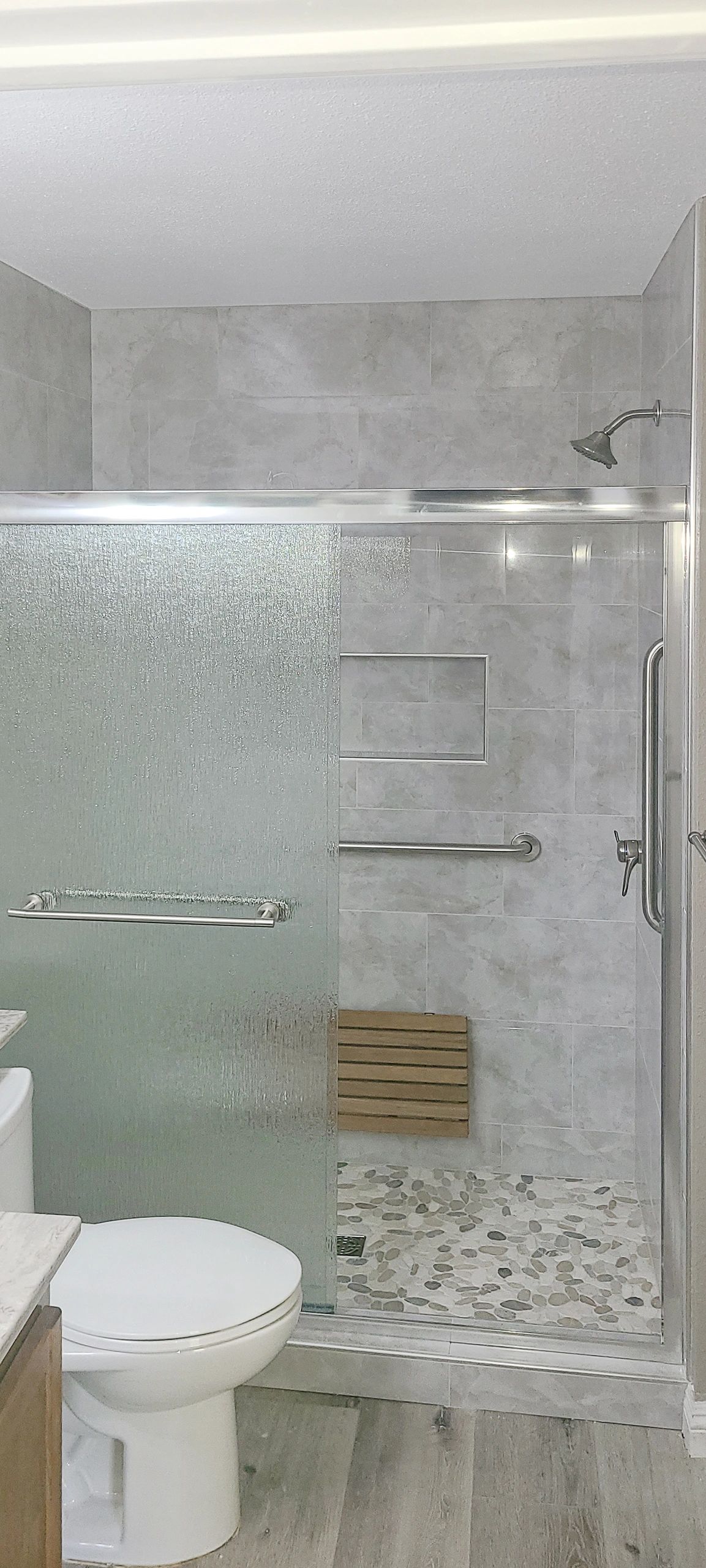 Shower walls and floor tiled, sliding shower door installed, teak fold down seat, grab bars