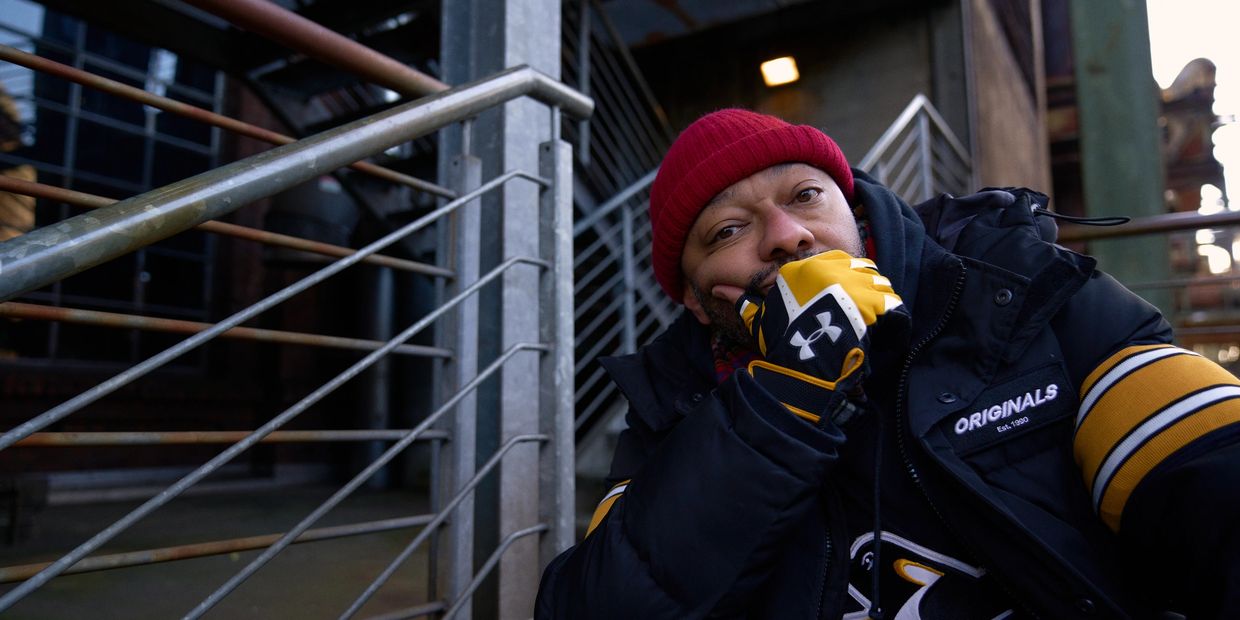 Man in warm clothing and gloves, sitting thoughtfully by metal railings.
