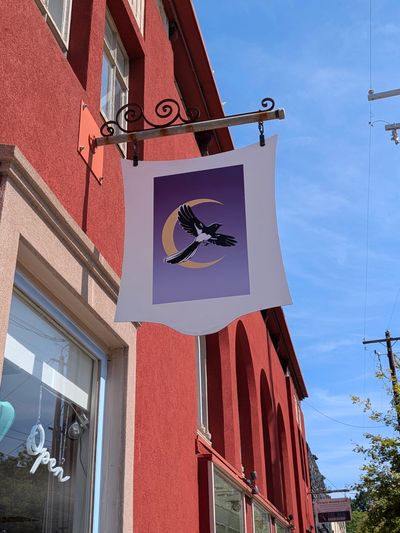 Hanging sign with bird and crescent moon on red building.
