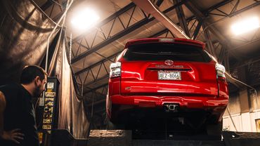 Vehicle inspection before rustproofing with an SUV elevated on a hoist in a professional warehouse.