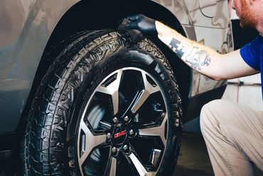 Man with tattoos wiping down and polishing brand new GMC tires after a fresh deep clean auto detail.