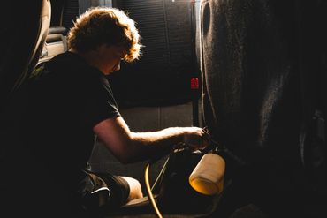 Man sitting inside a dimly lit vehicle spraying down seats and detailing the car interior.