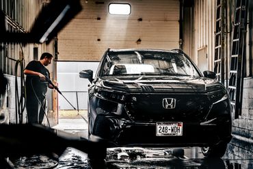Man hosing down freshly detailed and washed black Honda SUV