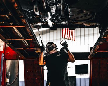 Man wearing respirator mask looking at undercarriage of a vehicle while applying rustproof.