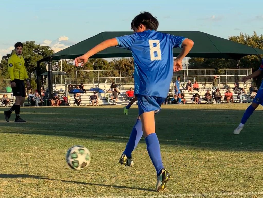 Young soccer player in blue jersey kicking the ball on the field.