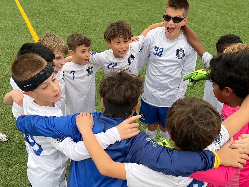 Youth soccer team huddling together in a circle on the field.