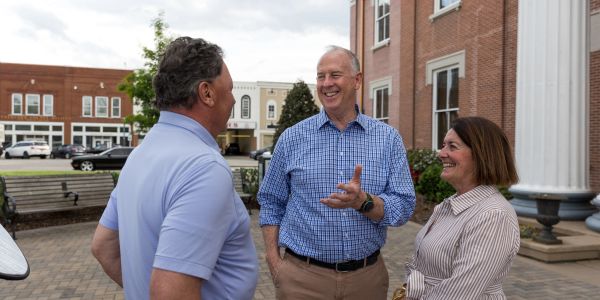 Three people happily chatting outdoors near a brick building.