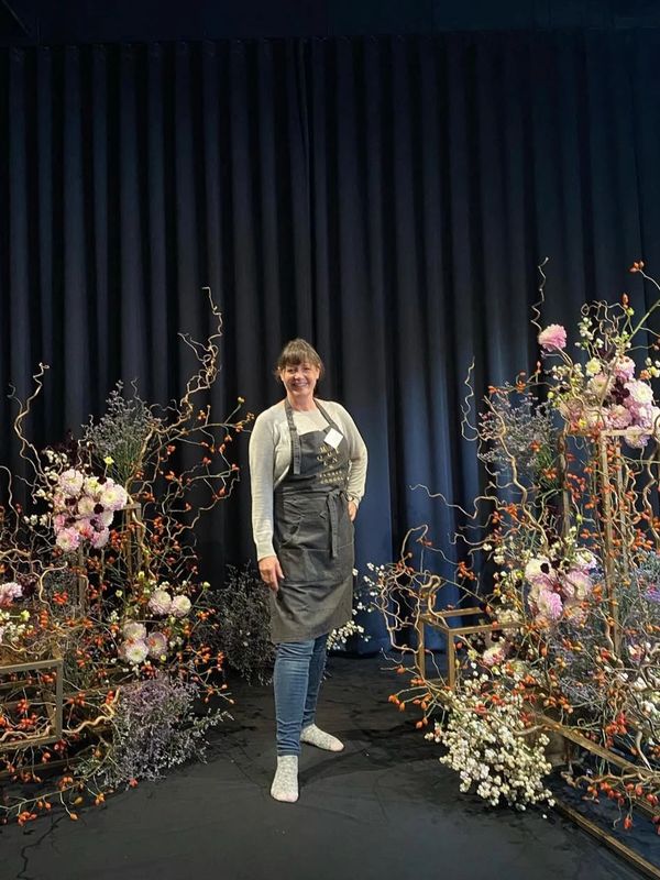 Woman in apron standing among decorative floral arrangements.