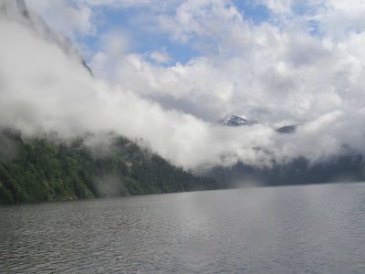 Fog rises alongside the mountains above the still waters of Misty Fjord, Alaska.