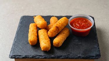 Mozzarella sticks with marinara sauce on a black slate plate.