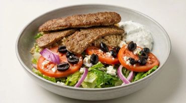 Greek-style salad bowl with meat, olives, and tzatziki sauce.