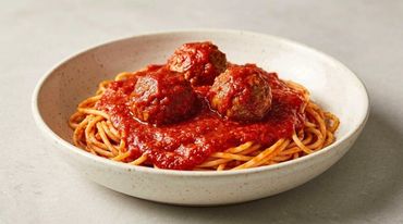 Spaghetti with meatballs and tomato sauce in a white bowl.
