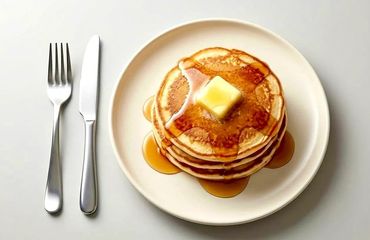 Stack of pancakes with syrup and butter on a white plate.