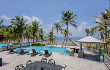 Luxurious beachfront pool area with palm trees and ocean view.