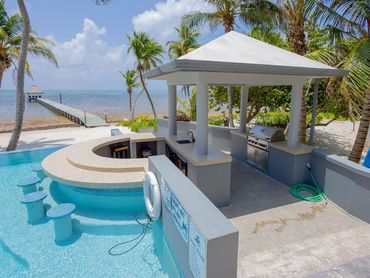 Tropical pool bar with seating, grill, and ocean view.