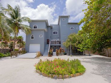 A large gray house with tropical plants and a circular flower bed in front.