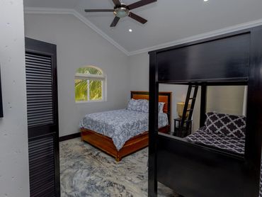 Bedroom with two beds, ceiling fan, and a window showing greenery outside.