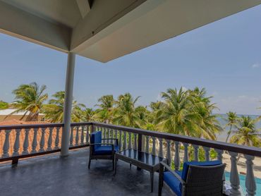 Balcony with blue chairs overlooking palm trees and ocean under a clear sky.
